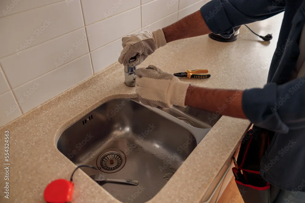 Gloved hands fitting a tap to a stainless steel kitchen sink