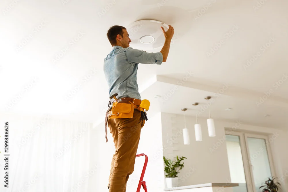 Electrician on a stepladder fitting a ceiling light in a bright living room