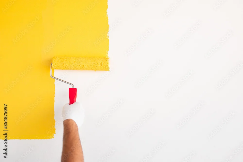 Paint roller applying yellow paint to a white wall